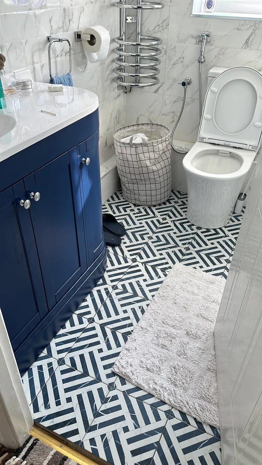 Modern bathroom installation with navy vanity, patterned floor tiles, and chrome towel radiator by MK Plumbing LTD.