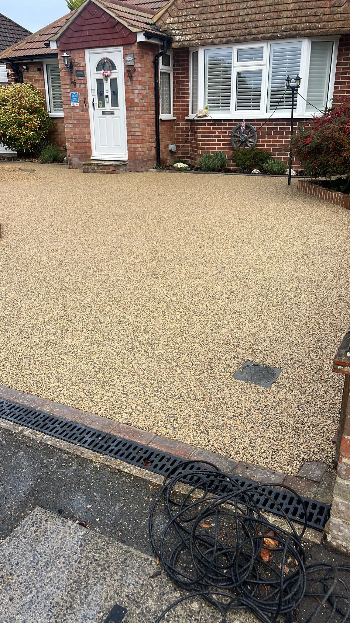 Newly laid light beige resin-bound driveway with linear drainage in front of a modern brick house in Tadley, Hampshire.