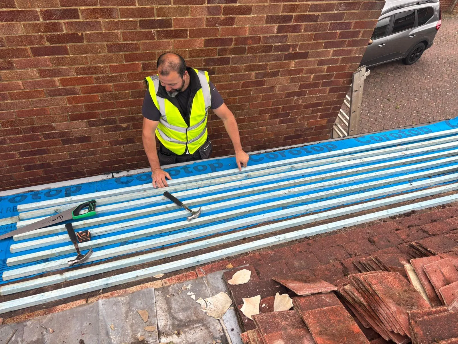 Roofer installing new wooden battens and blue underlay felt on a roof during a re-roofing or new roof installation project.