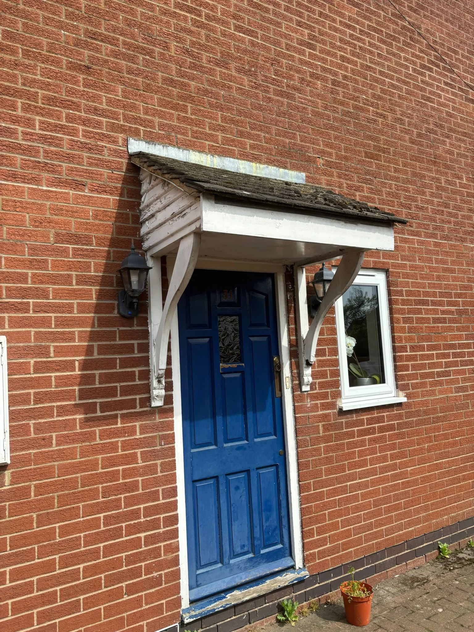 A blue front door with a small tiled porch canopy on a red brick house.