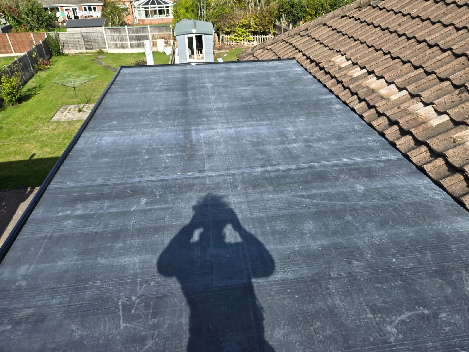 Newly installed dark grey flat roof on a residential property, showcasing a smooth, waterproof finish alongside a traditional tiled roof.