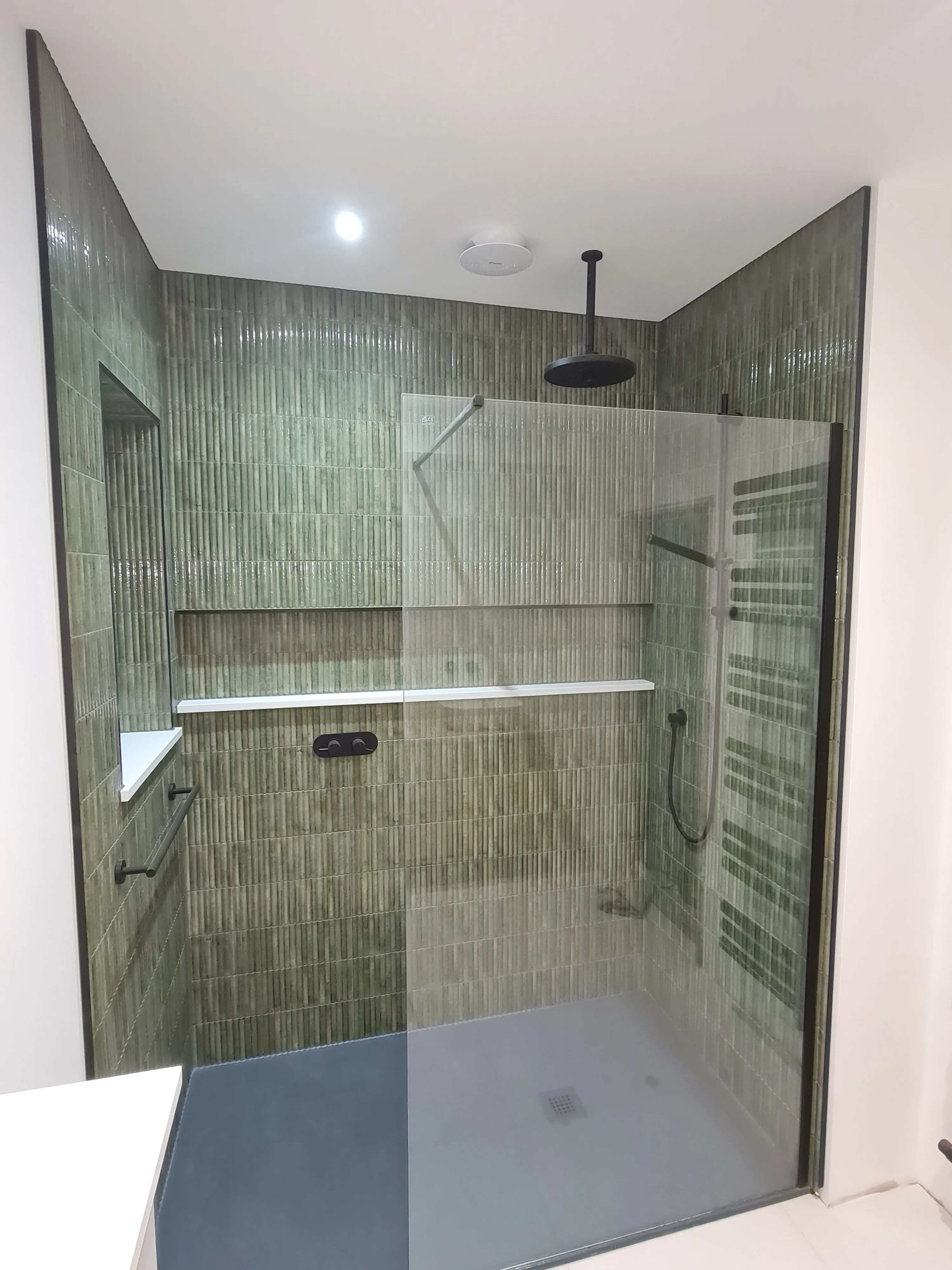 Bespoke luxury walk-in shower with green tiles and black fixtures by Sands & Vossen