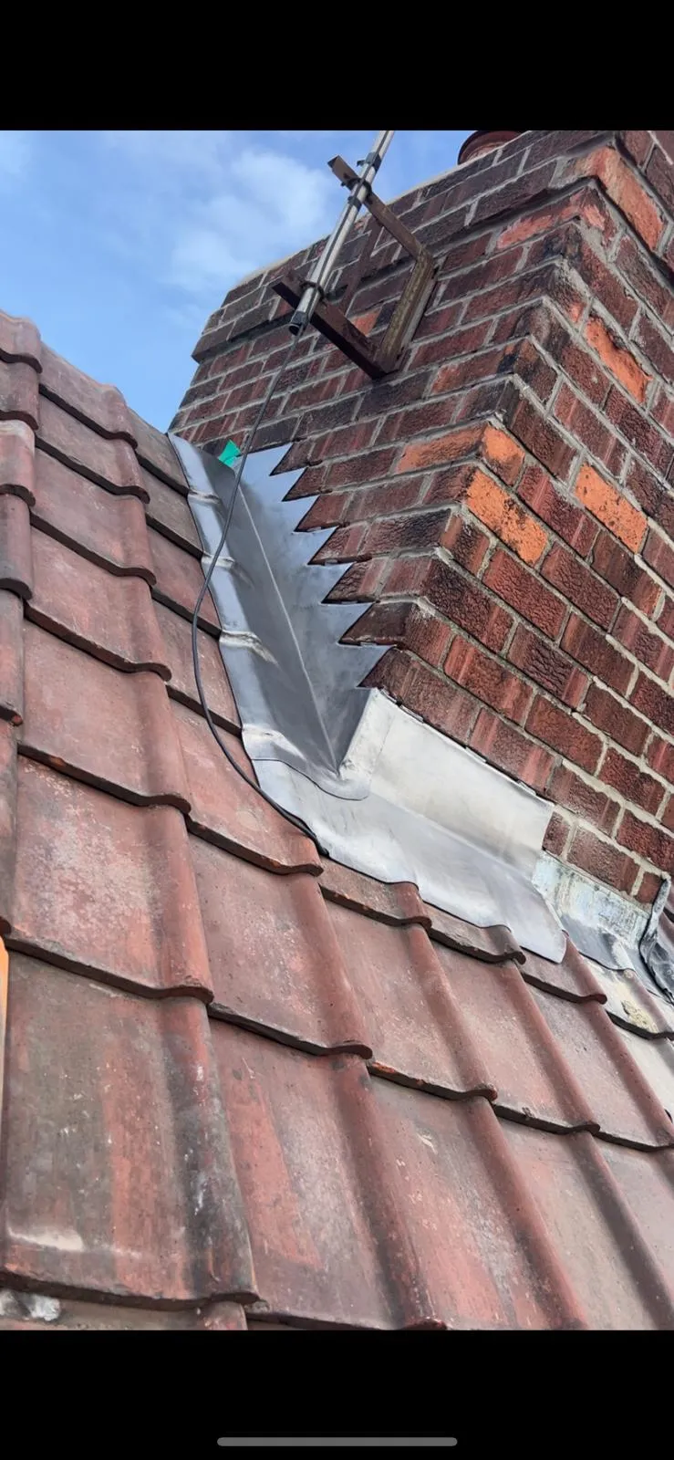 Expert leadwork and flashing installed on a red tiled roof around a brick chimney in York.