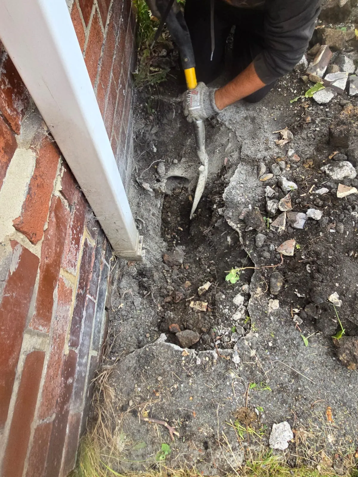APJ drainage engineer digging a trench next to an exterior wall to repair a collapsed drain.