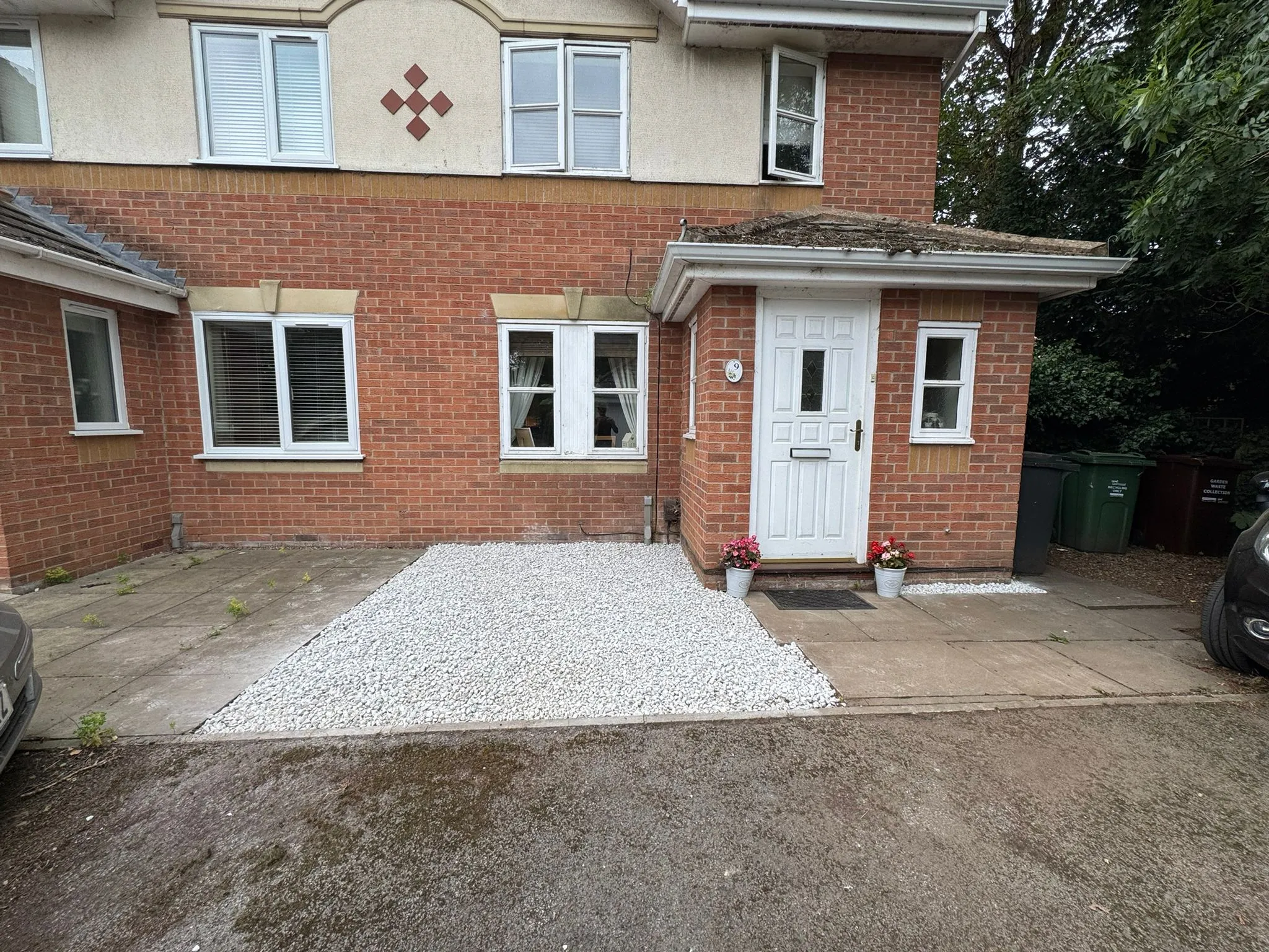Before shot of a residential front garden with old paving, white gravel, and a white front door, awaiting landscaping transformation.