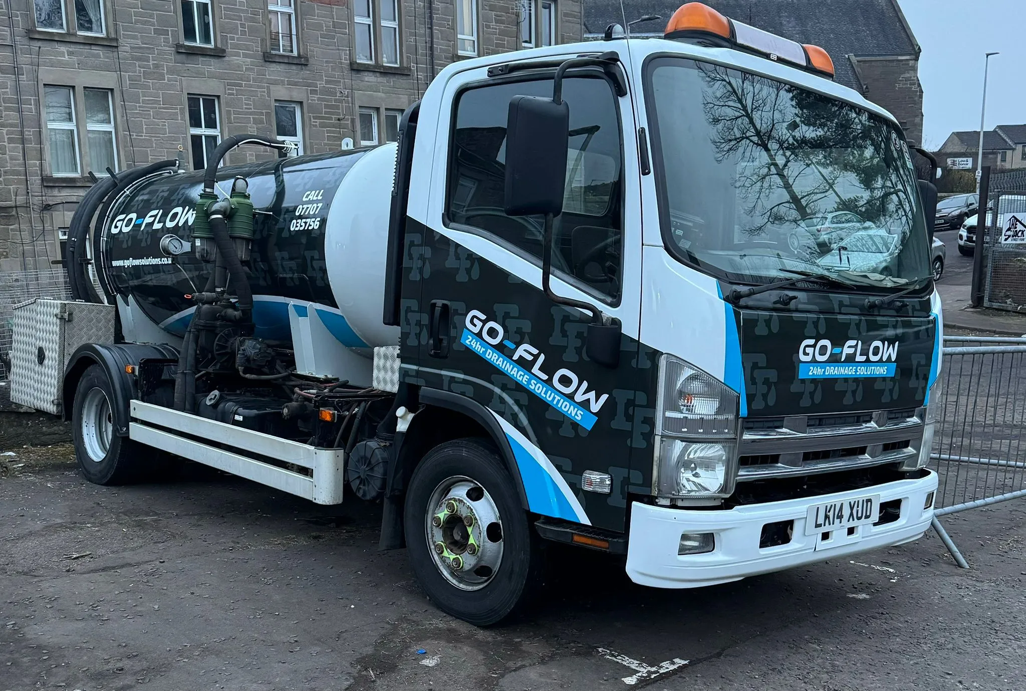 A white and dark green Go Flow Solutions Edinburgh tanker truck with 'GO-FLOW 24hr DRAINAGE SOLUTIONS' written on its side, parked on a street.