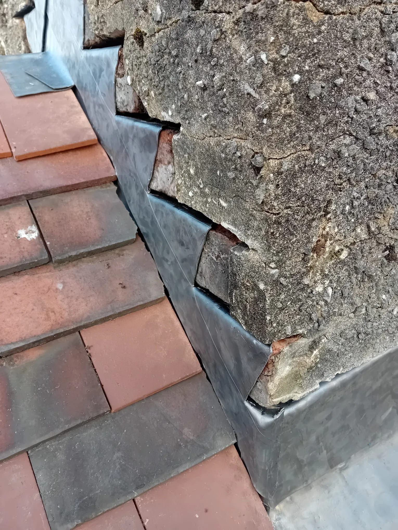 Expert chimney flashing repairs showing stepped lead flashing on a brick wall and tiled roof in Gloucestershire.