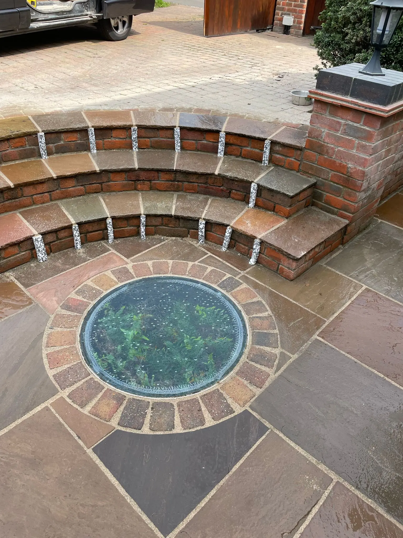 A bespoke sandstone patio installation with curved brick steps and a circular glass feature