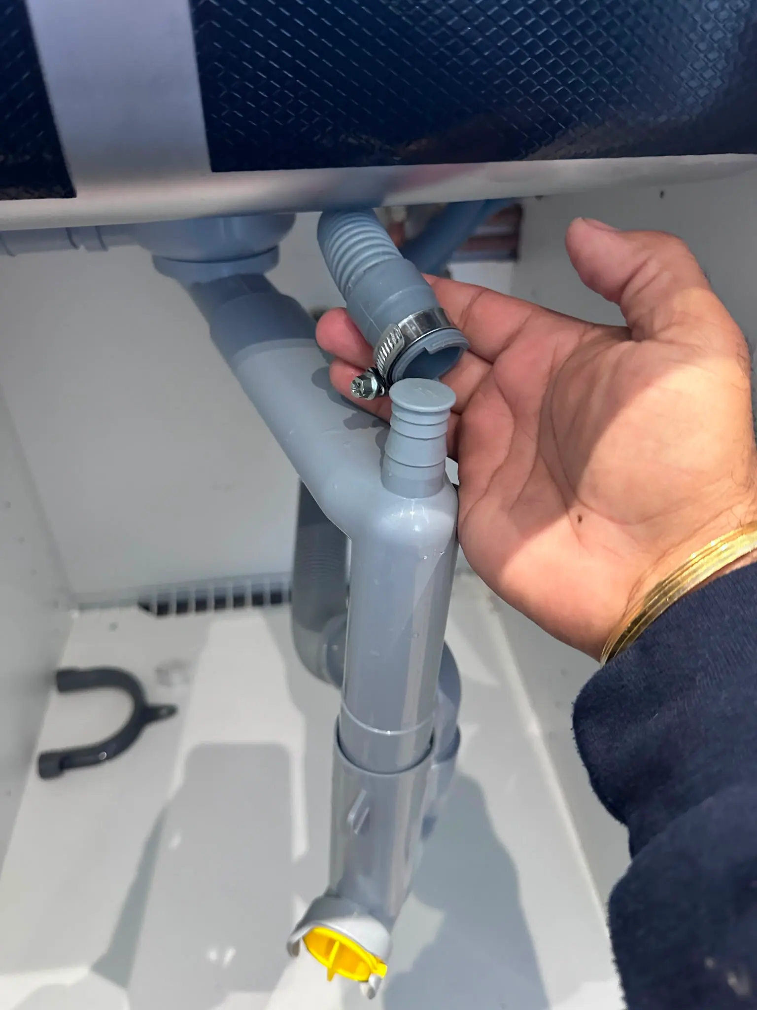 Plumber holding a disconnected appliance waste hose near a sink trap under a kitchen sink