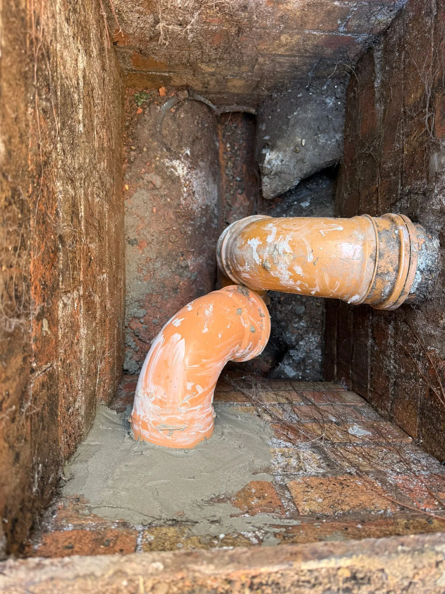 New orange drainage pipes and pipework installation inside a brick manhole chamber