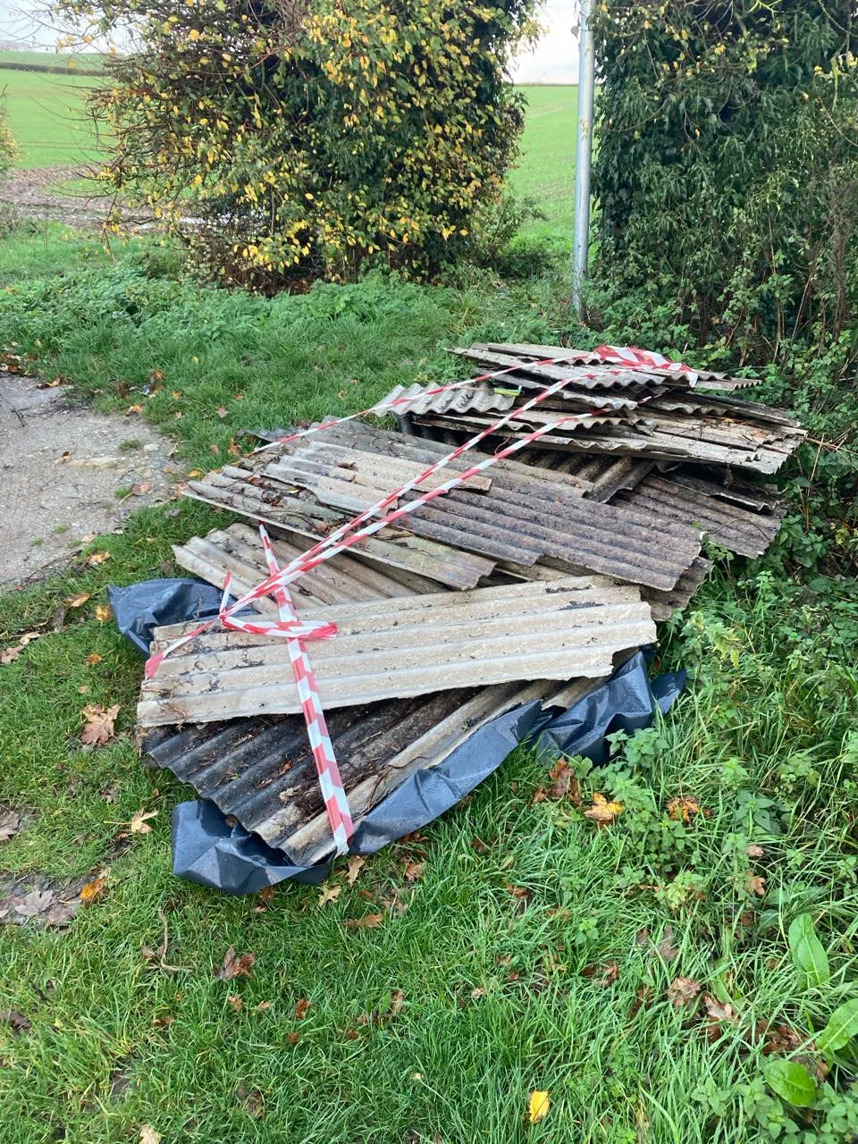 Pile of asbestos garage roof sheets with hazard tape on grass