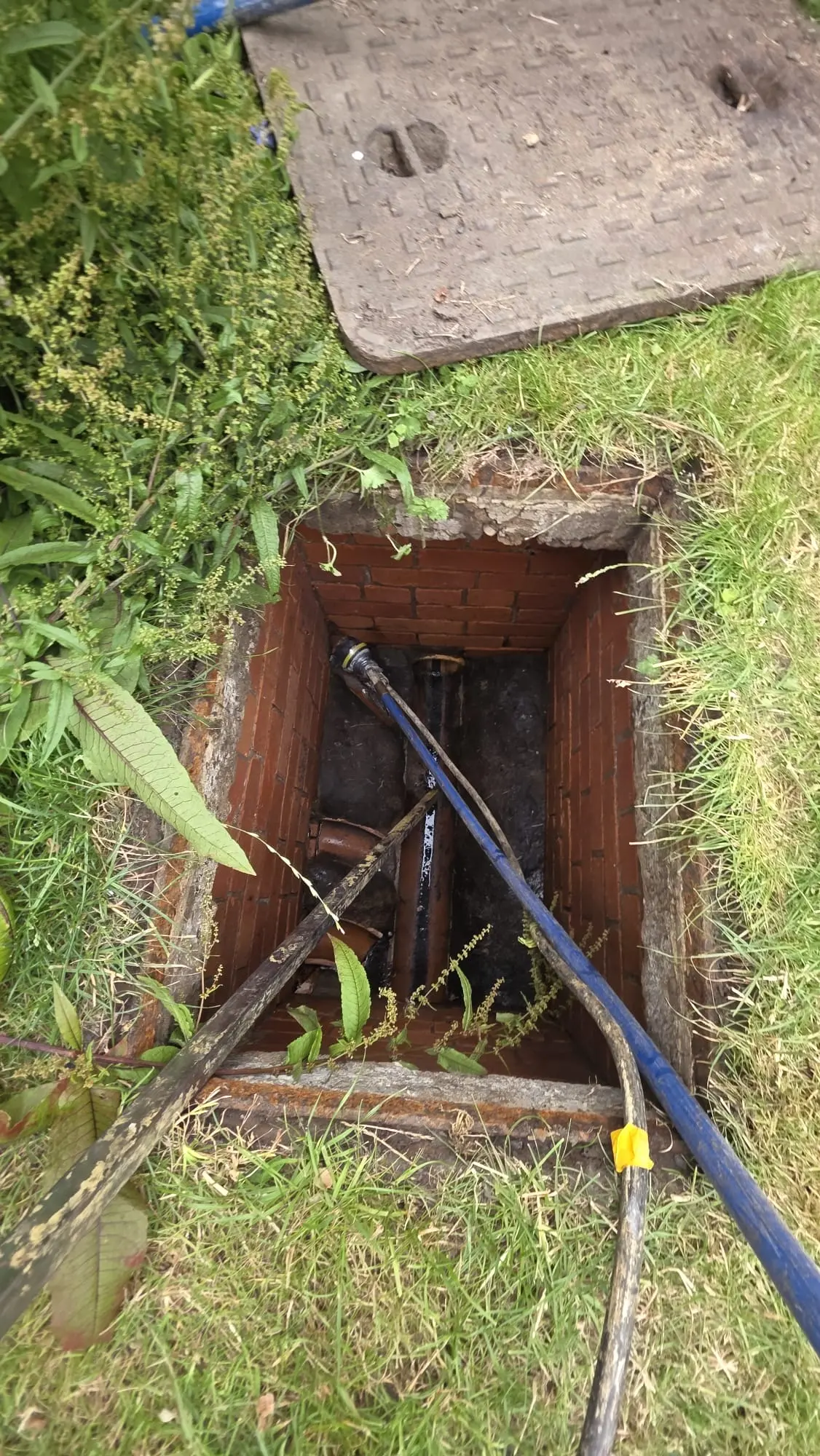 High-pressure water jetting hose and drainage rods inserted into an open residential manhole for emergency drain unblocking.