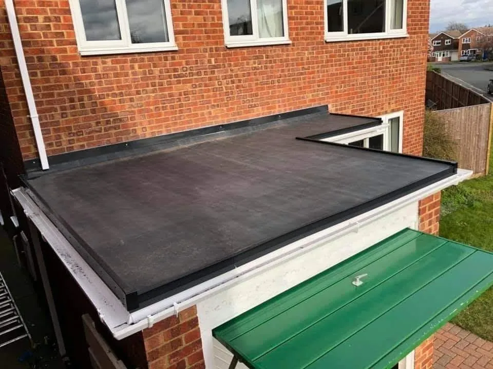 A close-up view of a modern flat roof installation on a brick house extension, showcasing the clean lines of the new roofing material and white UPVC guttering.