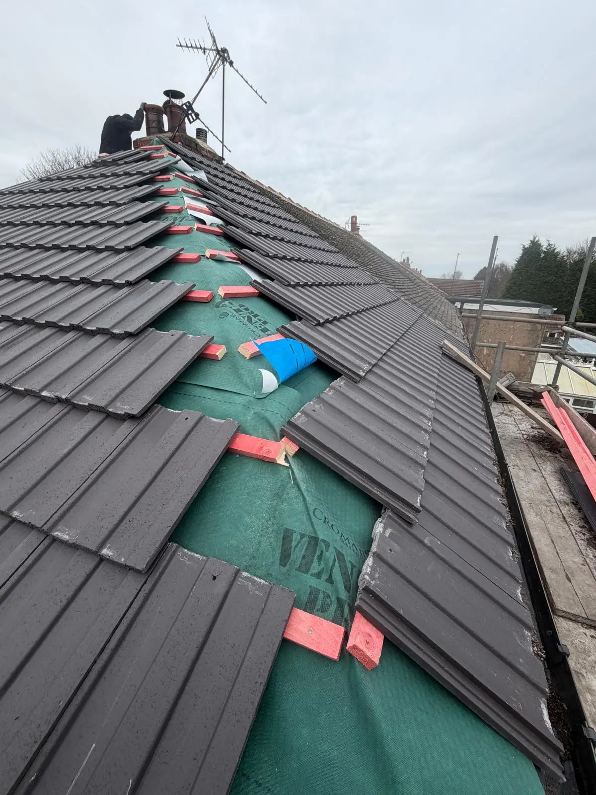 A picture of a tiled roof repair in progress showing exposed underlay and battens