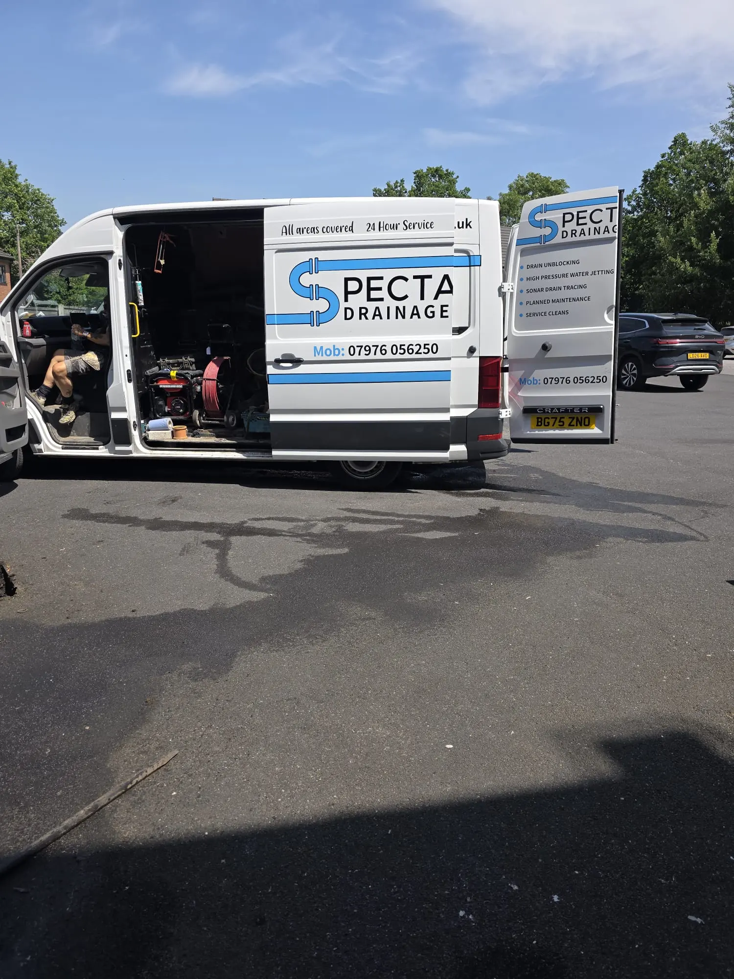 A white Spectra Drainage van with open doors showing equipment inside, parked on tarmac.