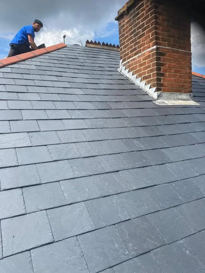 A roofer installing slate tiles and chimney leadwork on a house in Hampshire.