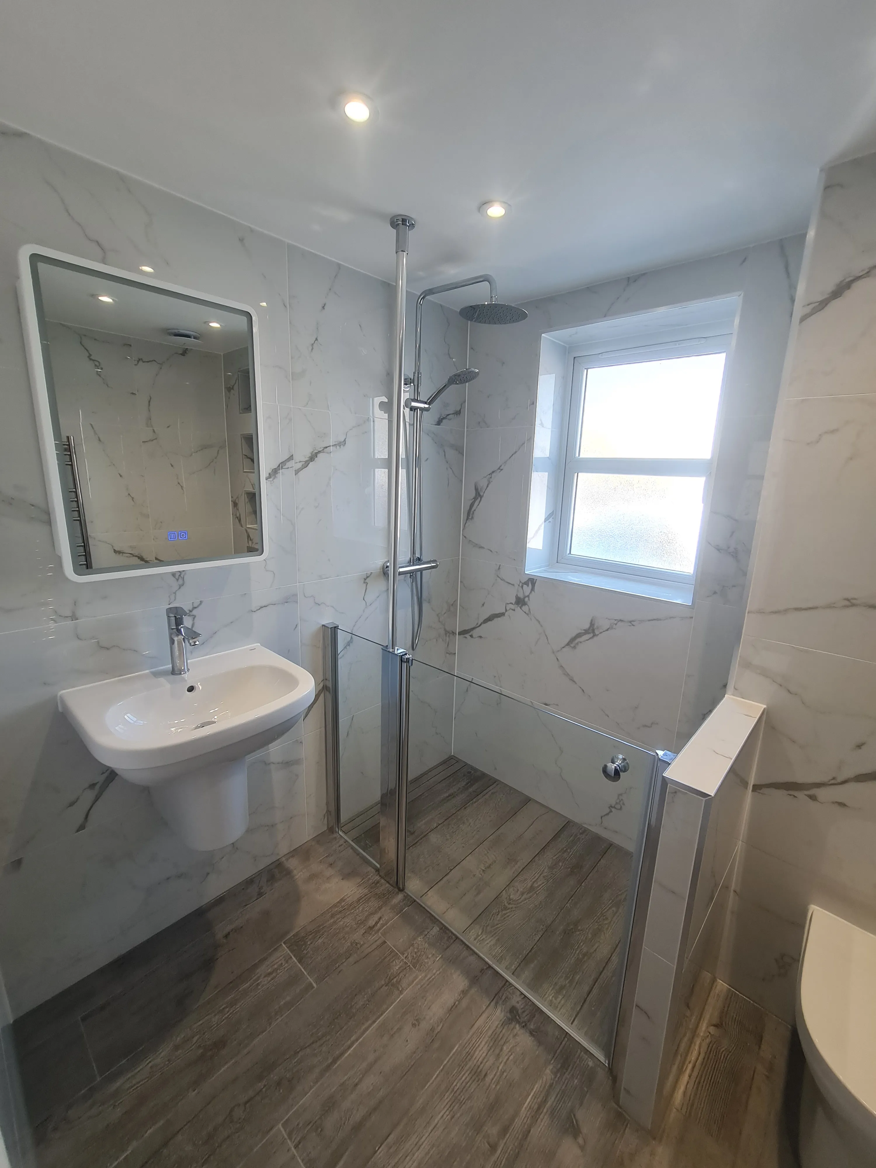 Bespoke luxury walk-in shower with marble-effect tiles and glass screen installed by Sands & Vossen