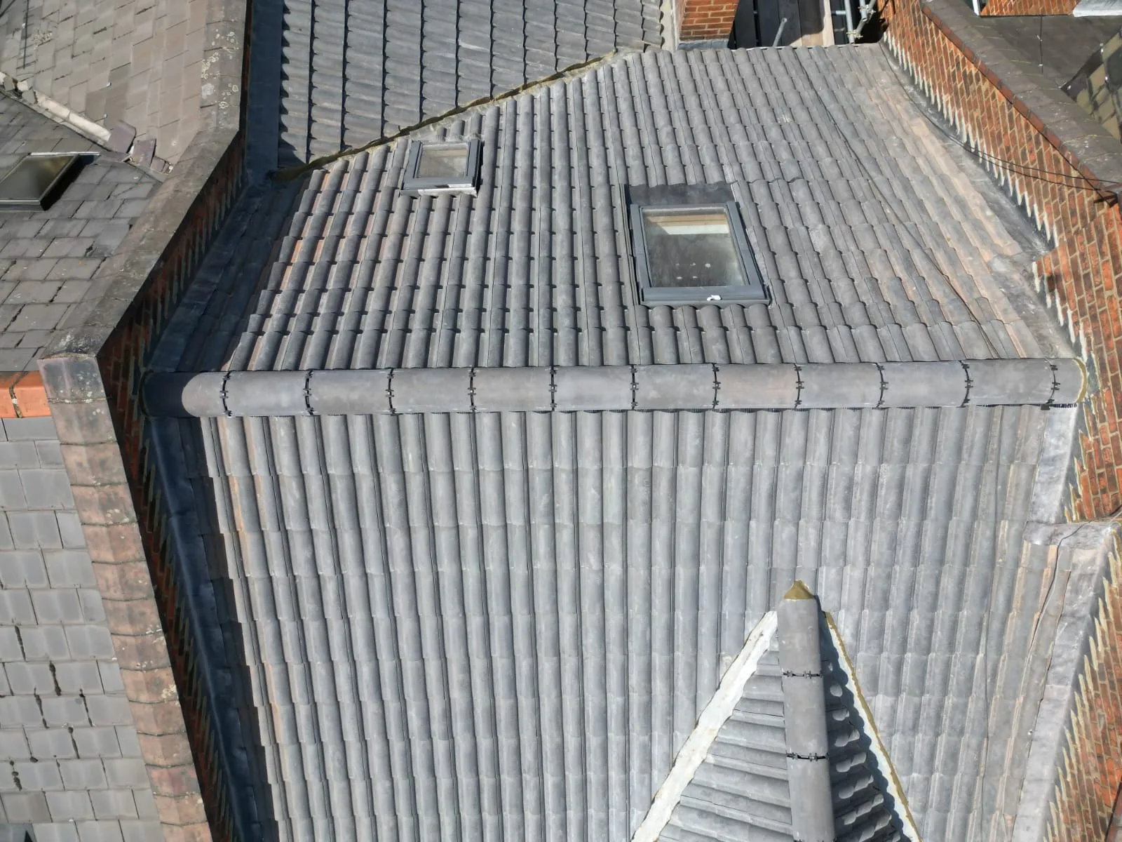 Aerial view of a modern grey tiled pitched roof with two roof lights, a new ridge, and clean lines, demonstrating expert roofing installation or repair.