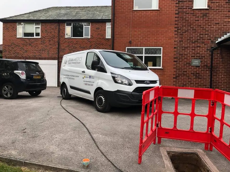Drain Medics van attending a residential property with an open manhole surrounded by red safety barriers