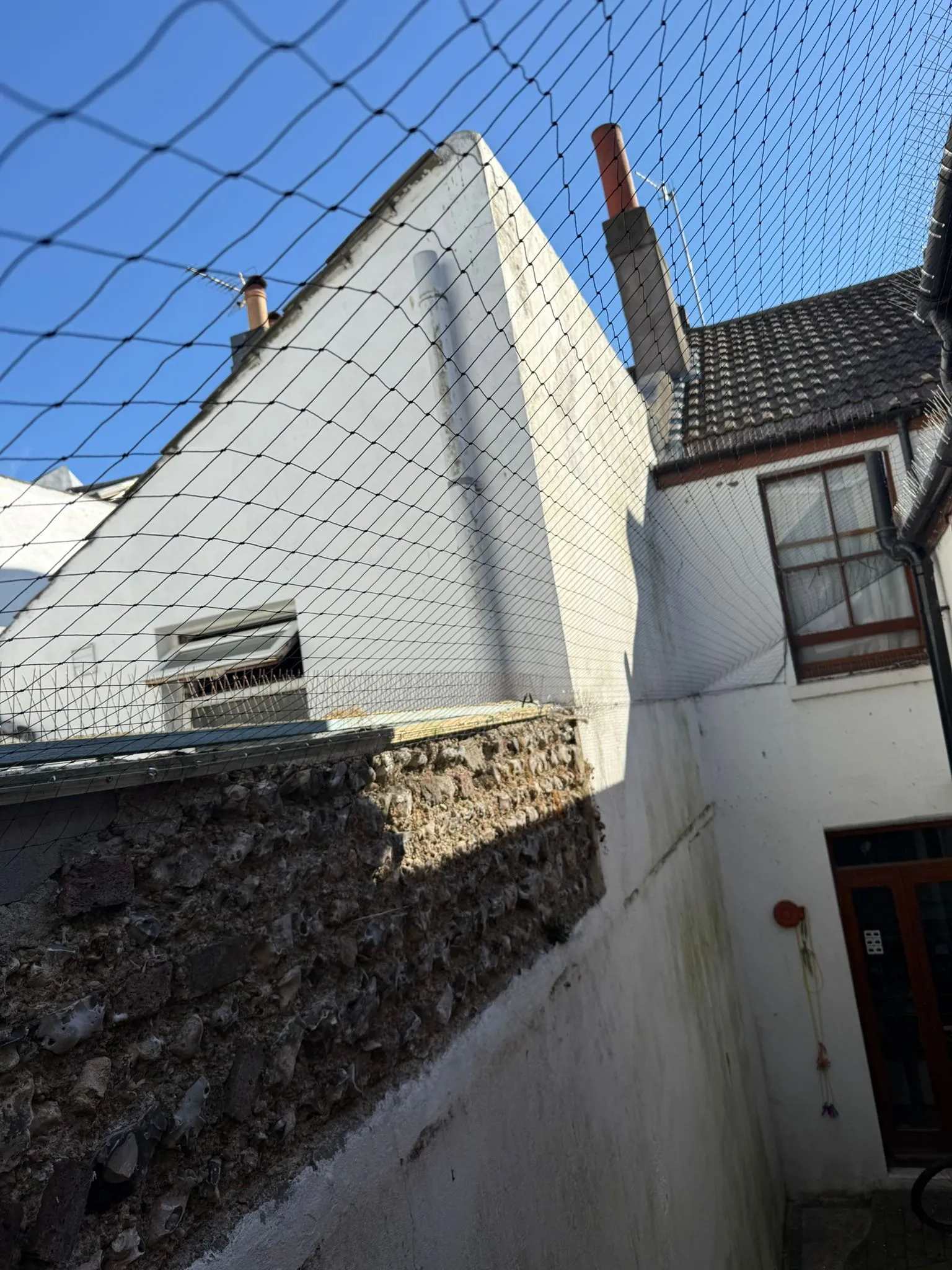 Bird control netting and anti-roosting spikes covering the exterior of a white residential building to prevent pigeons and seagulls from landing and nesting.