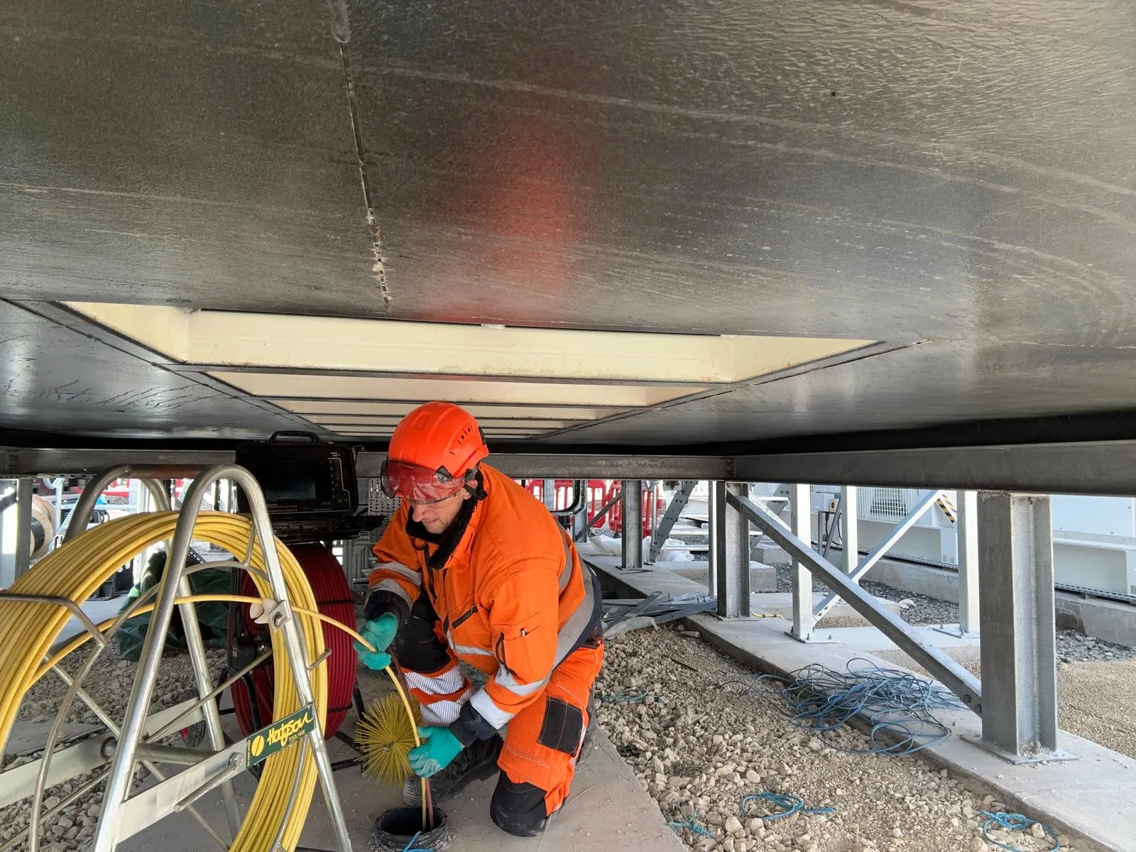 Drain Magic LTD engineer in high-vis overalls and hard hat, operating a mechanical drain descaling tool with a brush attachment, working on an external drain at a commercial site.
