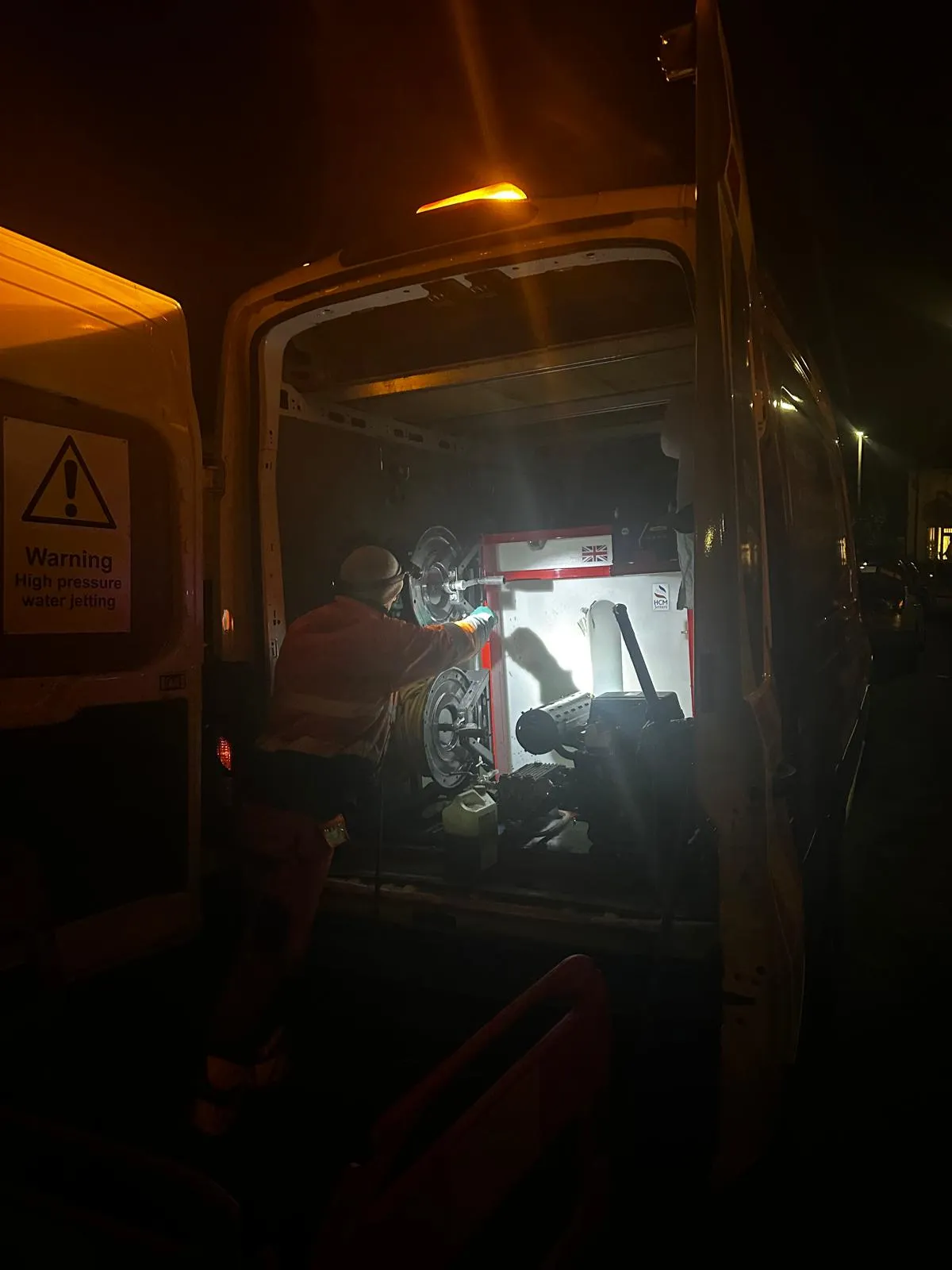 Drain Magic engineer using high-pressure water jetting equipment from a van at night to clear a blocked drain.
