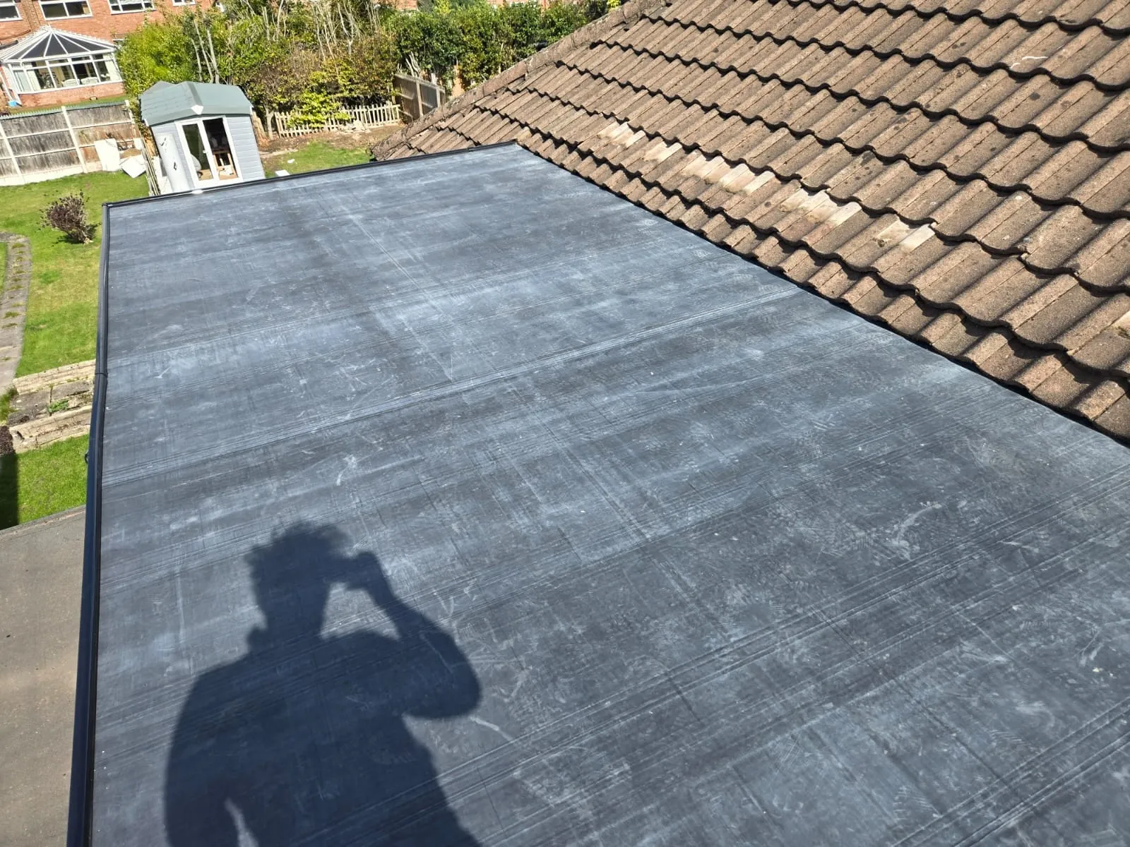 Newly installed dark flat roof meeting a tiled pitched roof on a residential property.