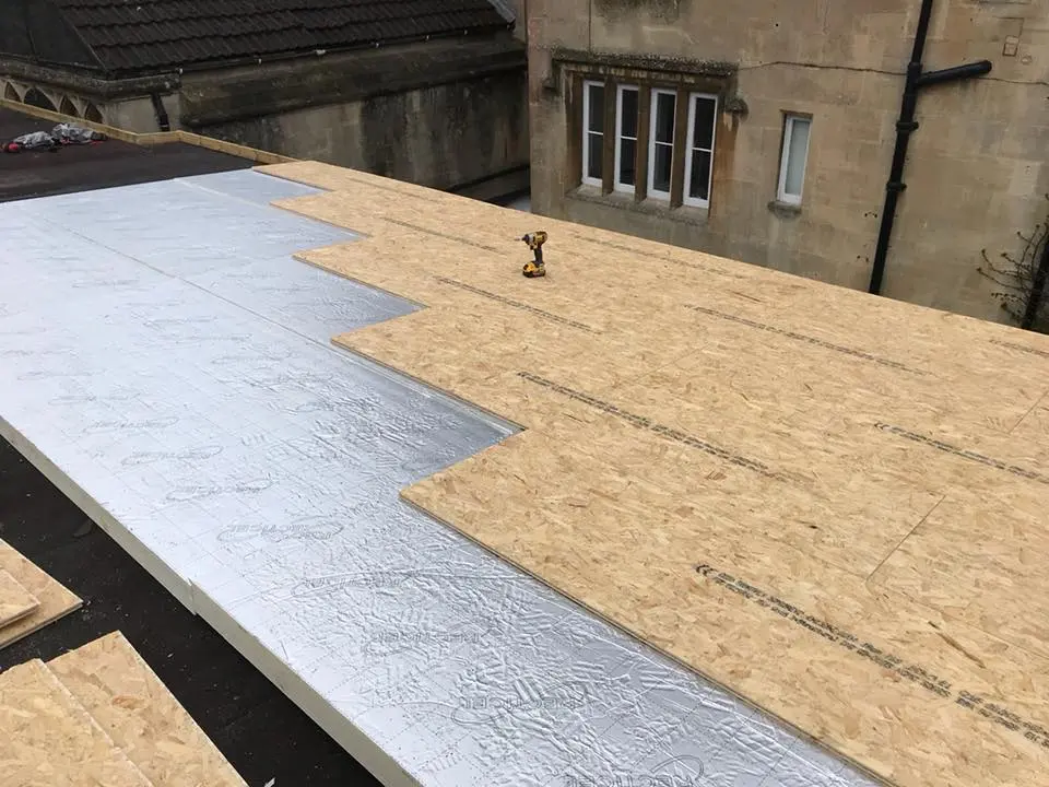 Flat roof installation process showing rigid insulation and timber OSB decking