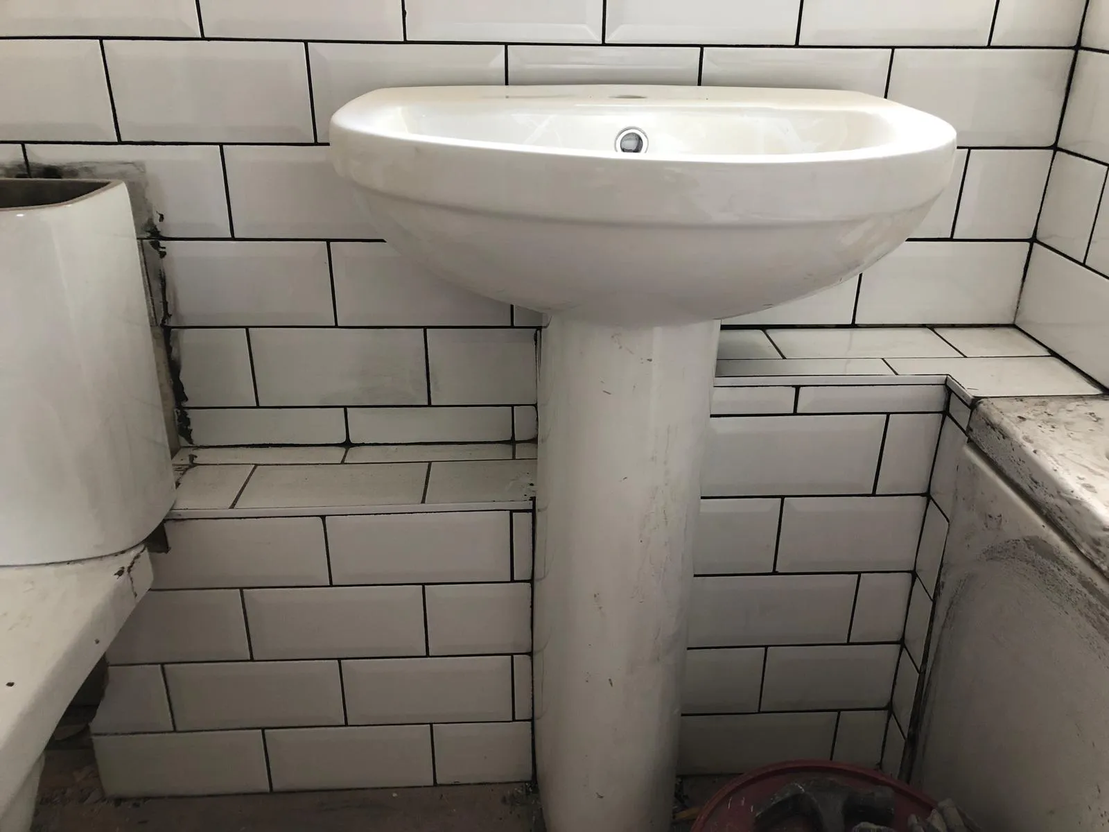 Pedestal sink and tiled walls in a bathroom under renovation.
