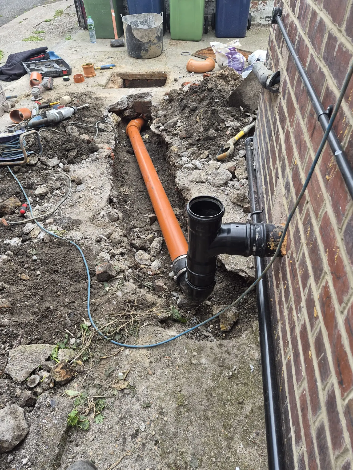 Excavation and installation of new uPVC underground drainage pipework alongside a brick building during a structural drain repair