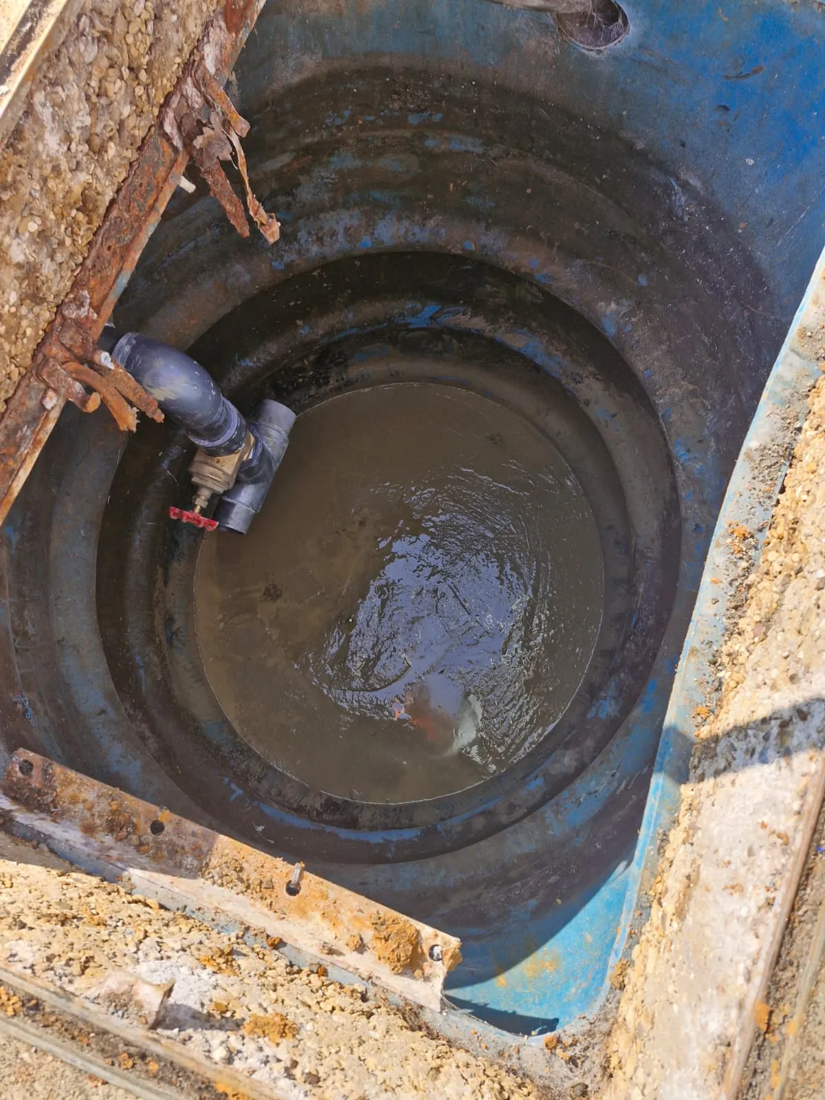 Looking down into a drainage chamber or pump station showing pipes and water.