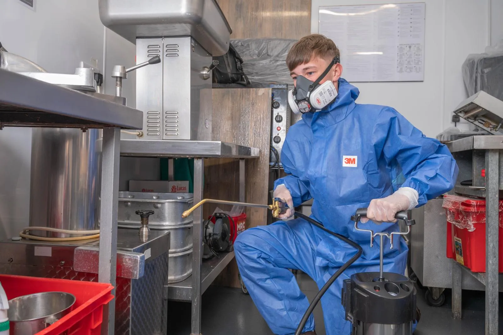 Professional pest control technician in full PPE treating a commercial kitchen in Harrogate.