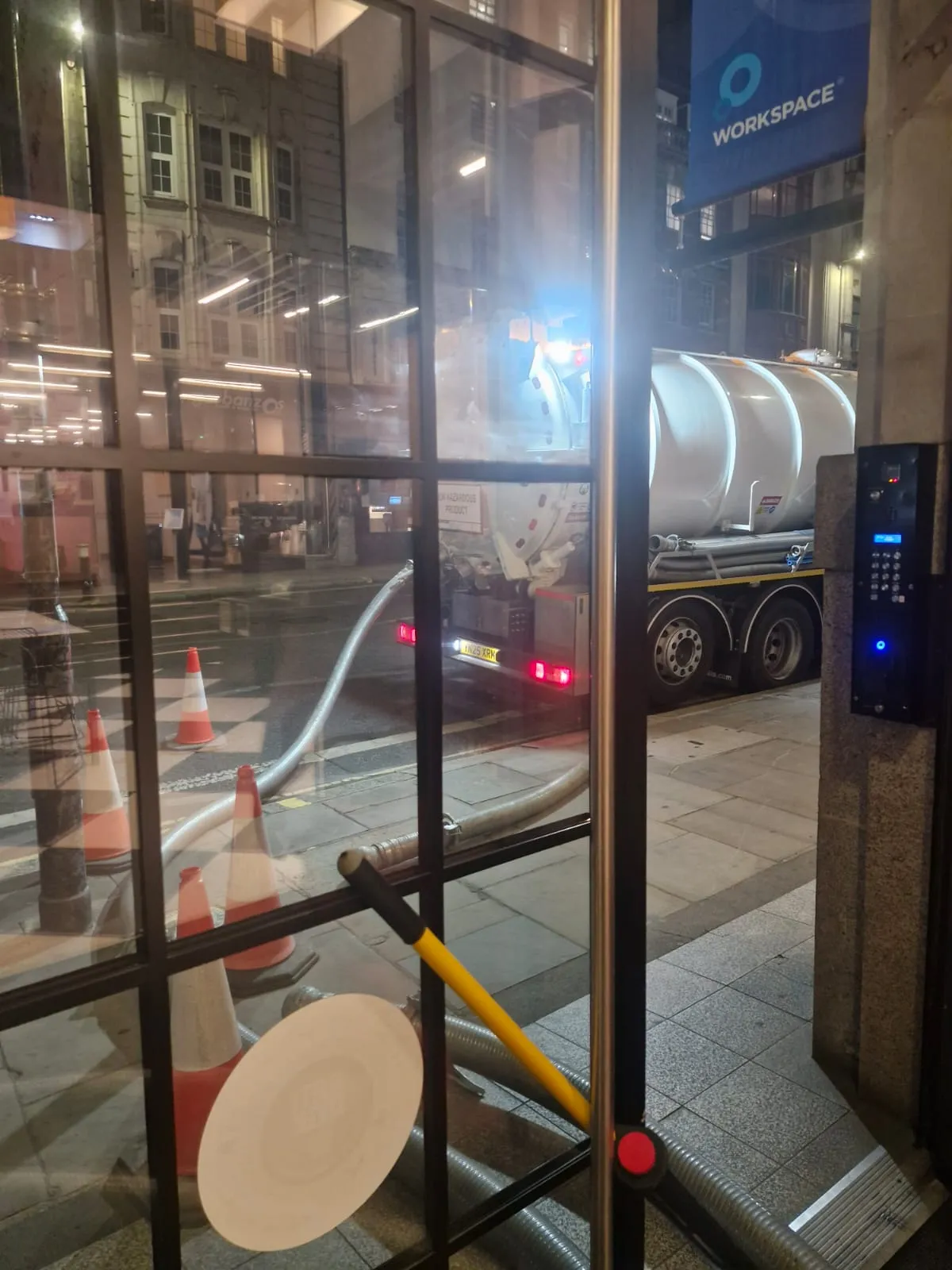 A white liquid waste tanker parked on a city street at night with suction hoses connected, representing professional liquid waste management services.
