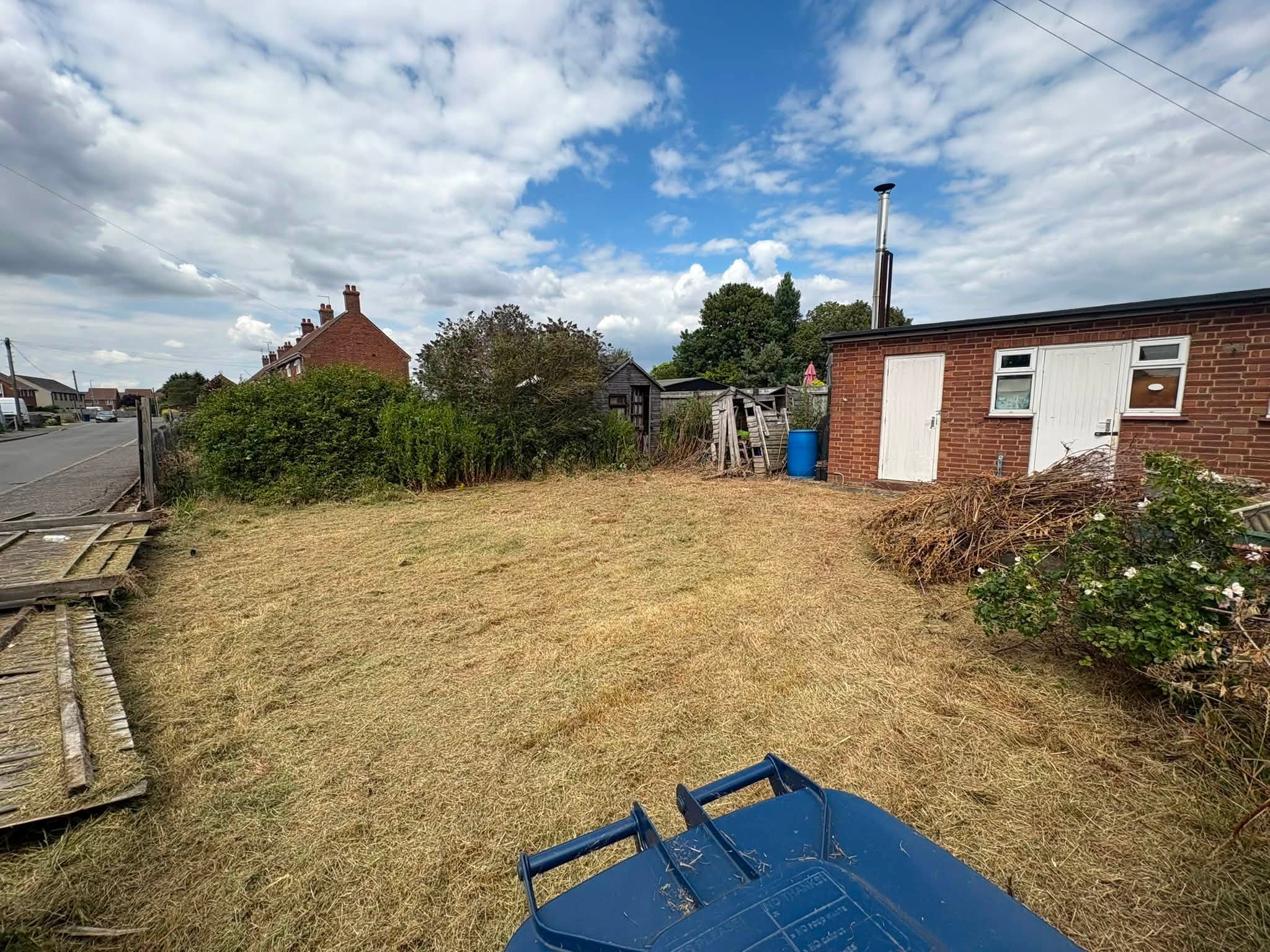 A large residential garden area in Huntingdonshire that has been recently cleared, showing cut grass and piled garden waste.