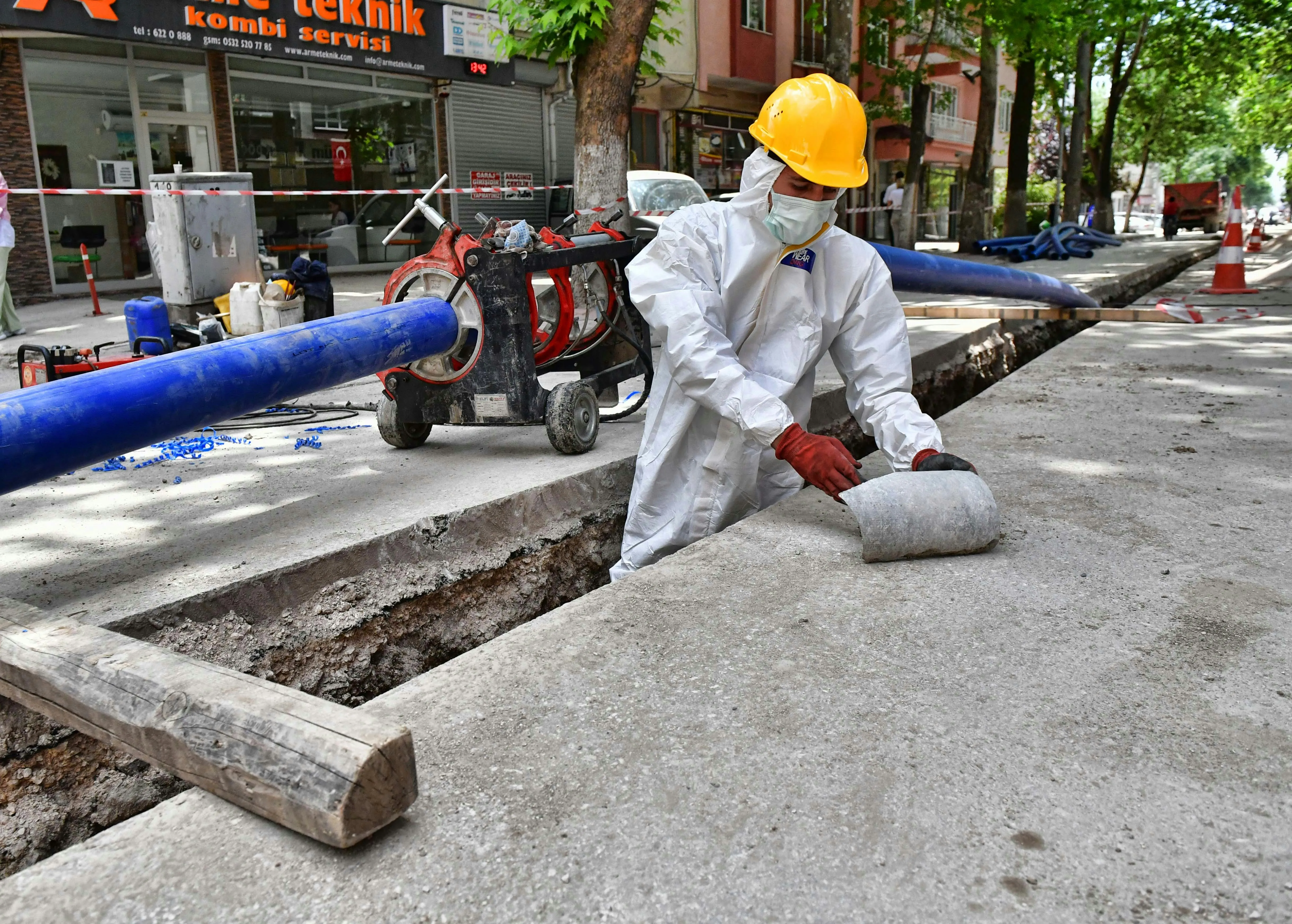 Professional worker in full PPE performing licensed asbestos removal in a street trench.