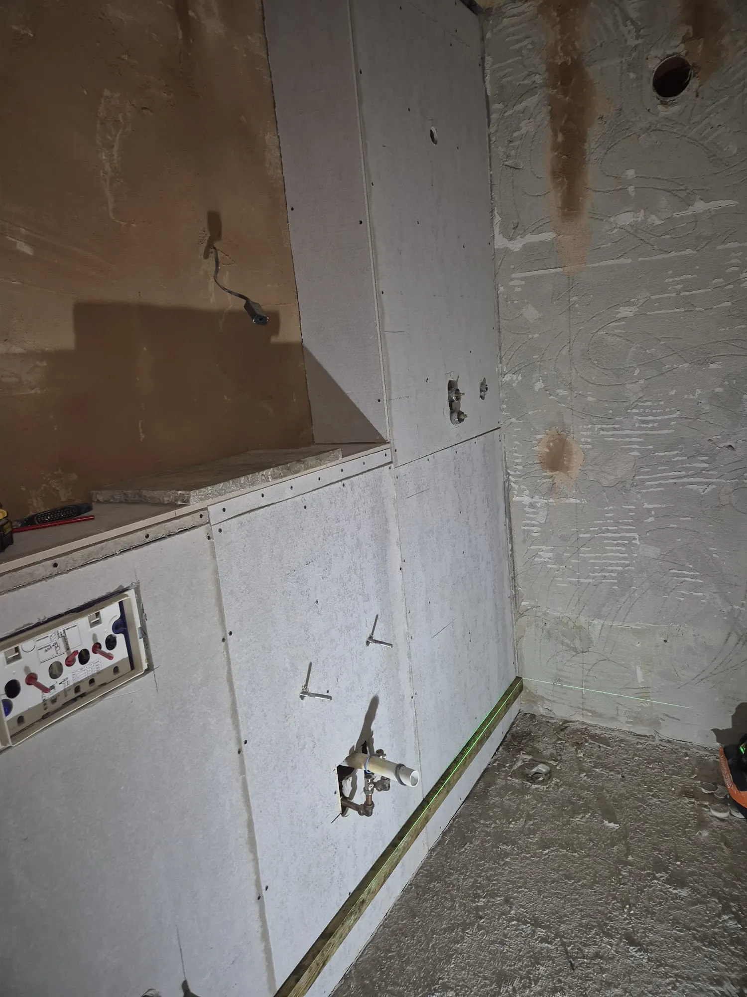 A construction site showing new plasterboard walls, exposed plumbing pipes, and electrical cables during a home refurbishment or renovation project.