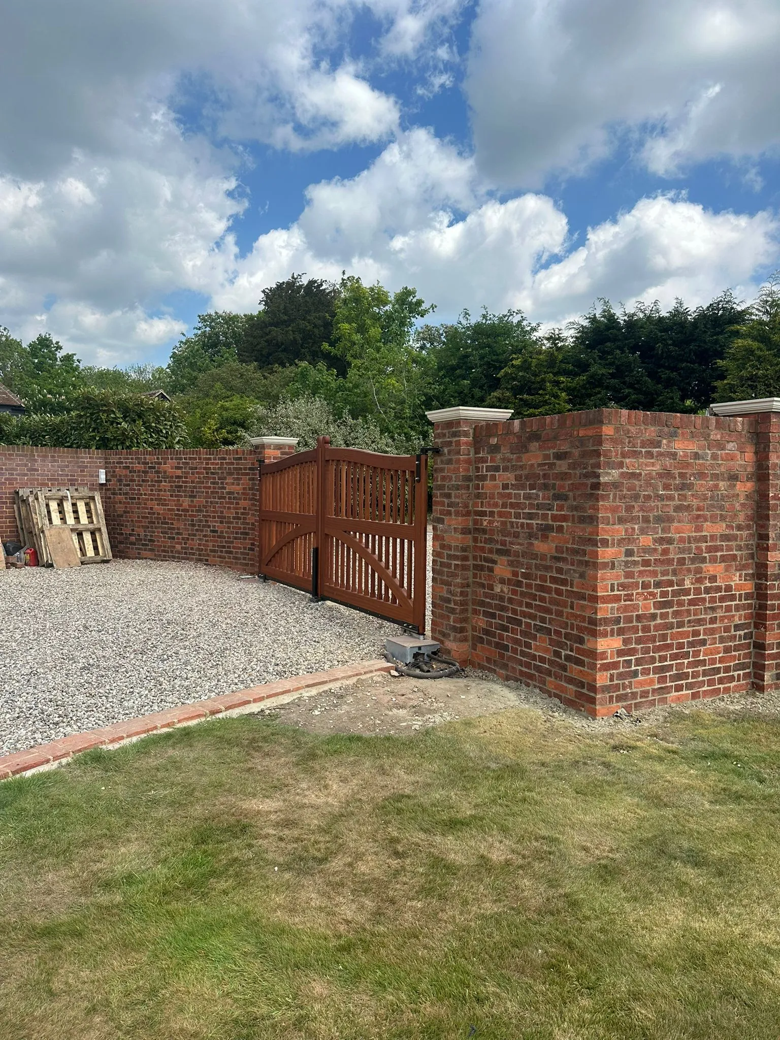 Newly installed red brick garden wall with decorative pillars and wooden driveway gates in Essex.