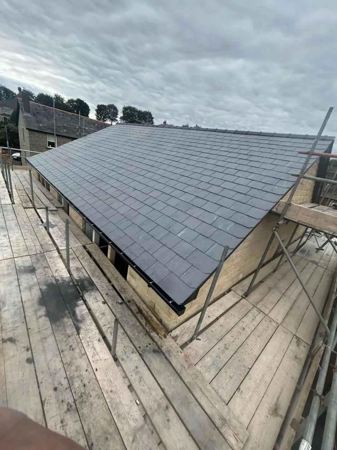A newly installed grey slate roof on a stone house in Holmfirth with construction scaffolding