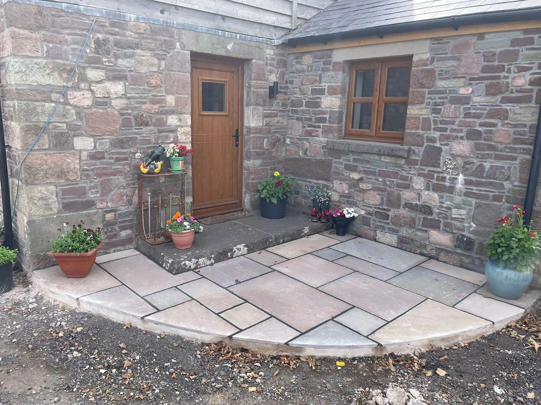 Natural stone patio laying and paving installation outside a traditional stone cottage by JDP Outdoor Solutions