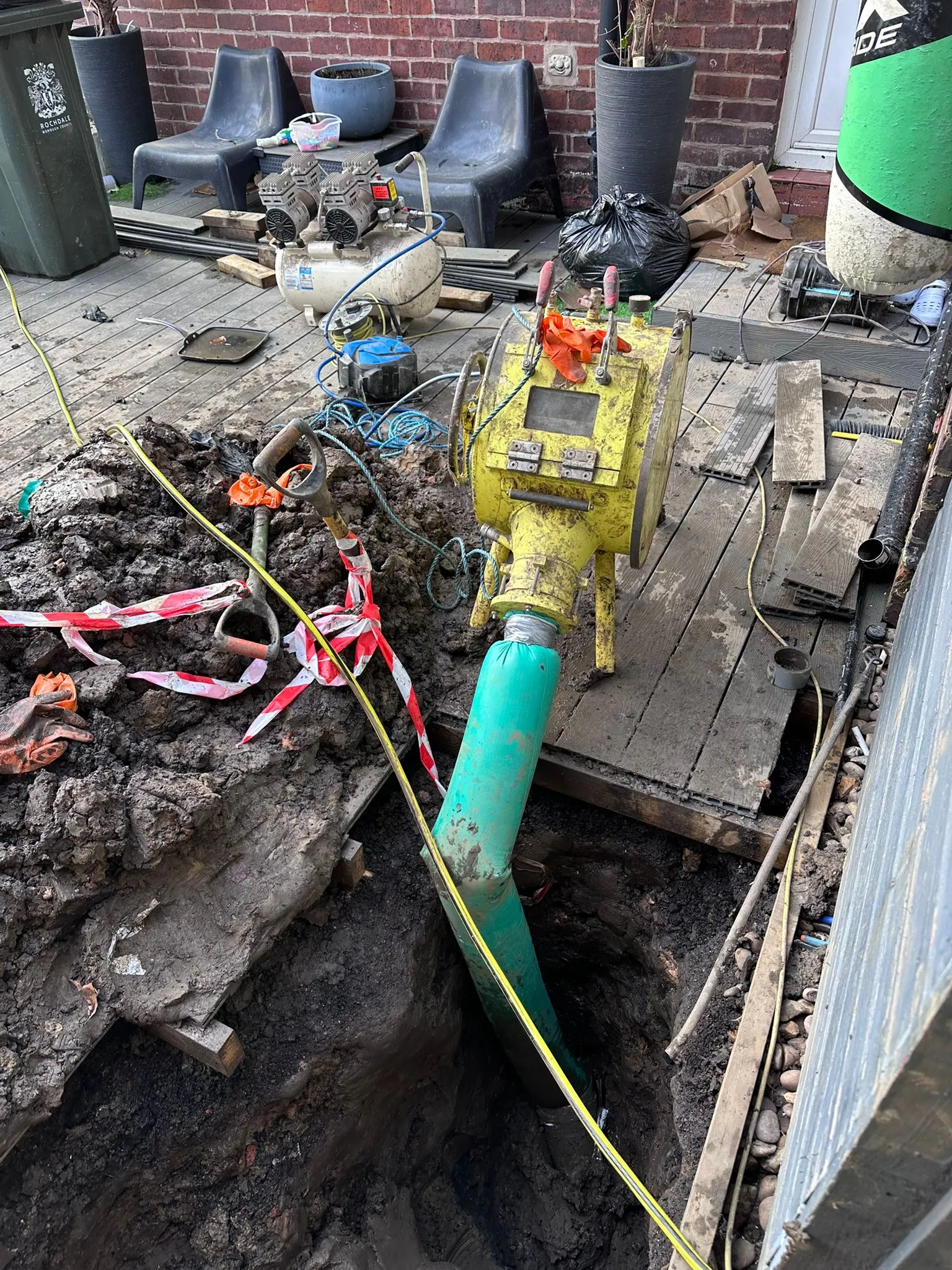 Professional drain lining repair showing inversion drum and liner in an excavation.