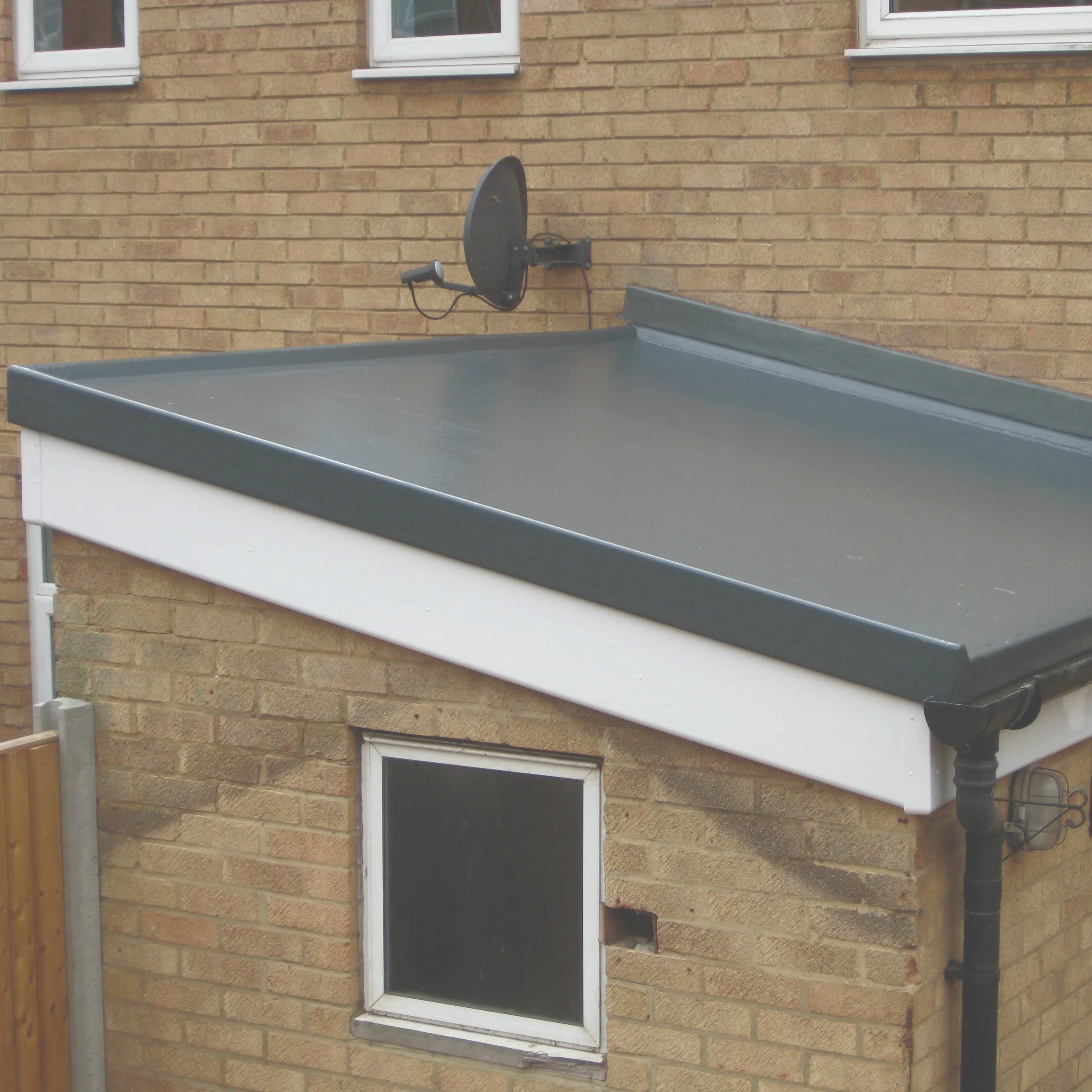 A new flat roof installation with dark grey GRP or EPDM membrane, white UPVC fascias, and black guttering on a brick extension.