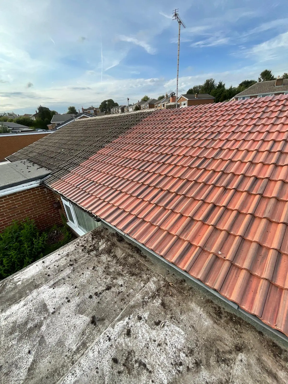 A comparison showing a newly installed red tiled roof next to old weathered roof tiles on a residential house