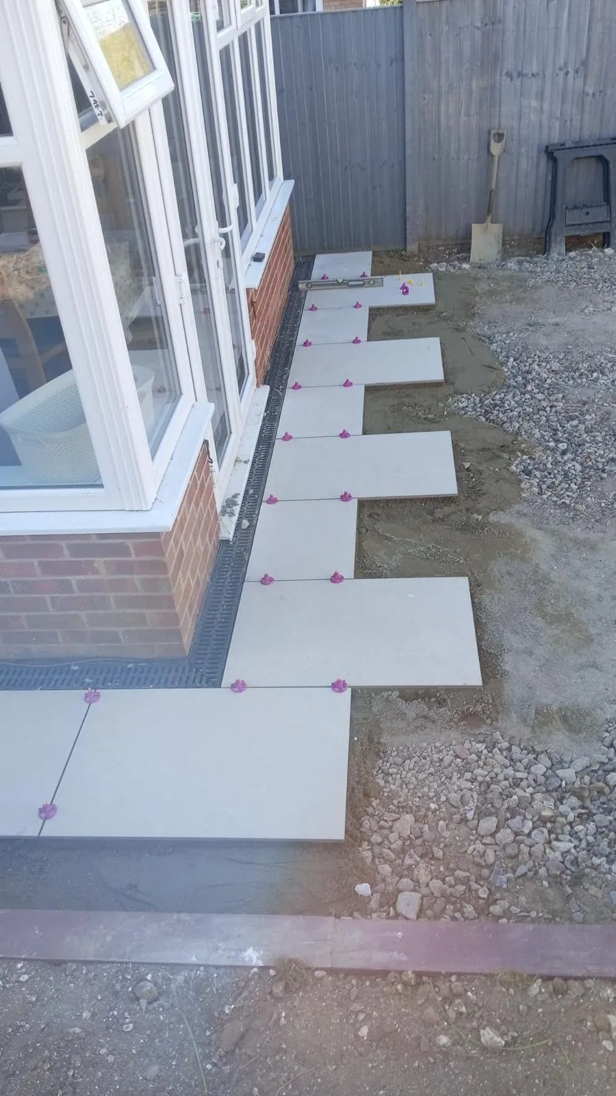 Paving slabs and linear drainage channel being installed next to a conservatory.