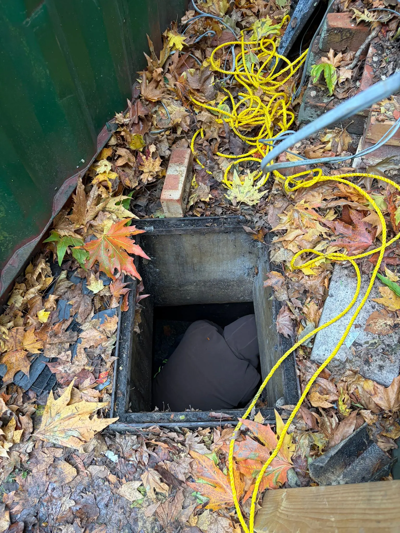 An open outdoor drain or manhole surrounded by leaves in Slough, showing a blockage.