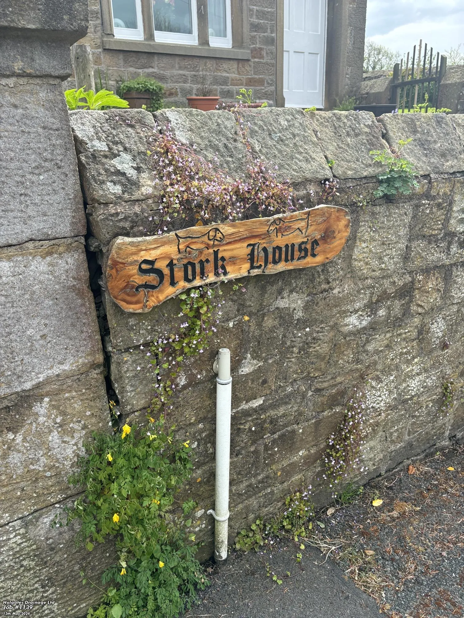 A wooden house sign for Stork House on a stone wall with an external drainage pipe, used for pest control drain inspections in Lancashire.