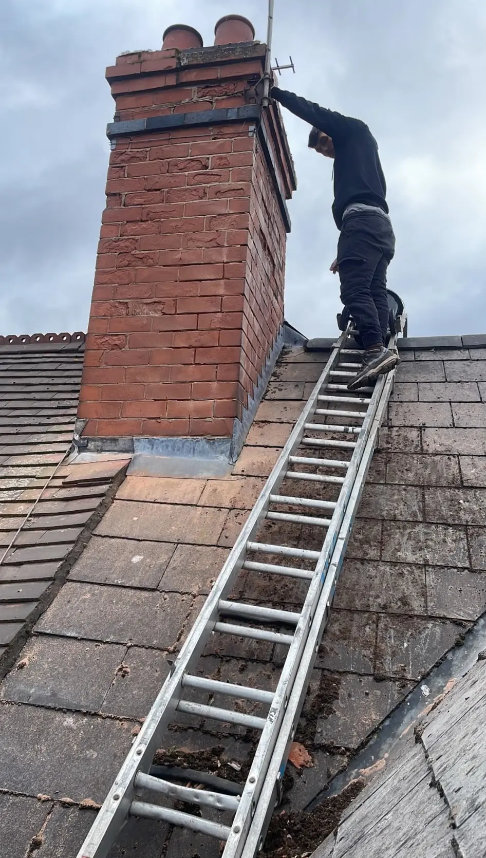 Professional roofer from Swift Property Solutions on a ladder inspecting a brick chimney for repointing and repairs in Northampton