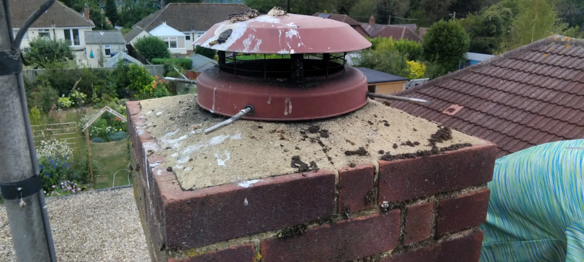 A close-up of a residential red-brick chimney stack and cowl requiring repairs and repointing