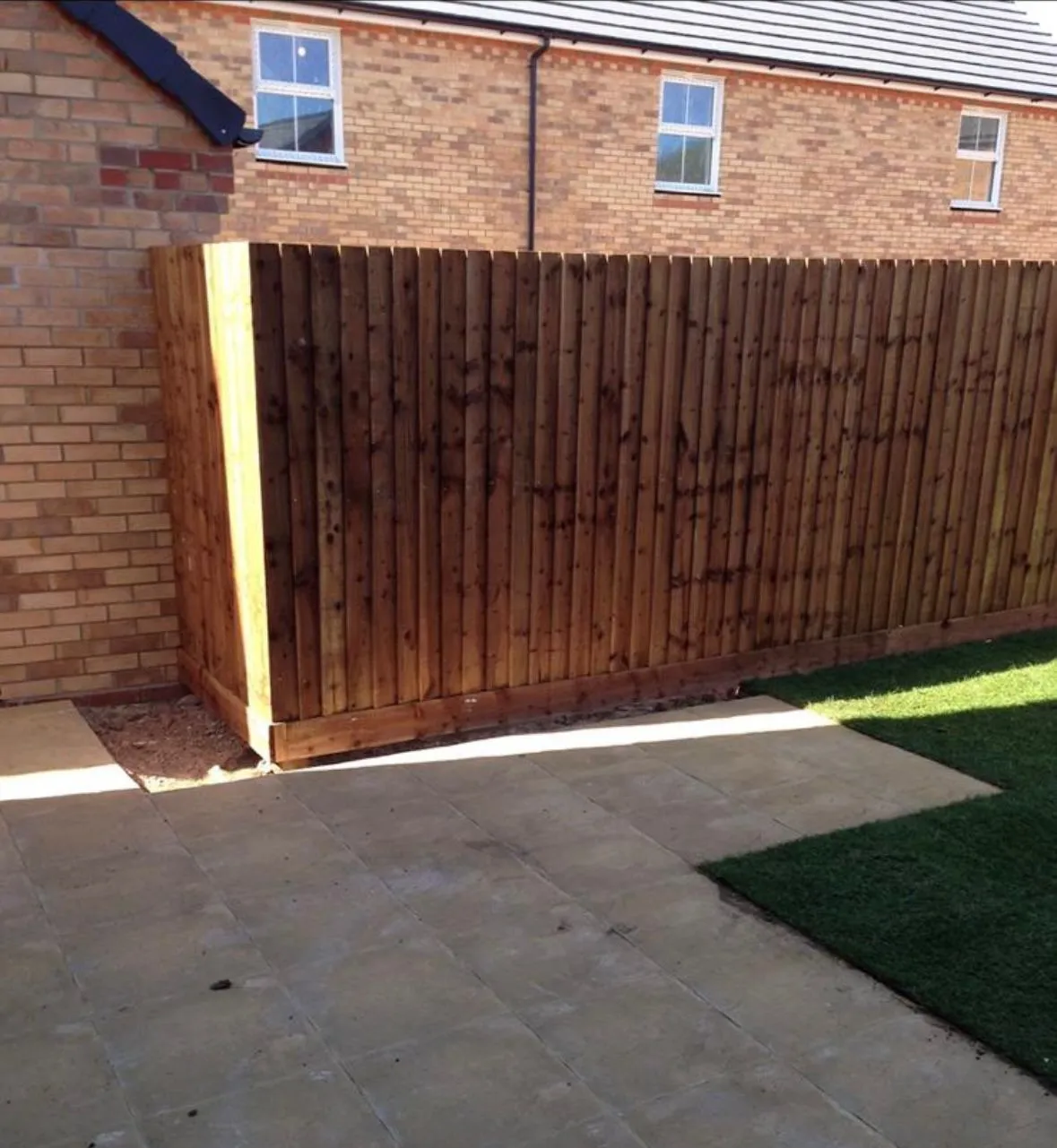 Newly installed closeboard wooden fence, paved patio, and artificial grass in a modern garden setting.