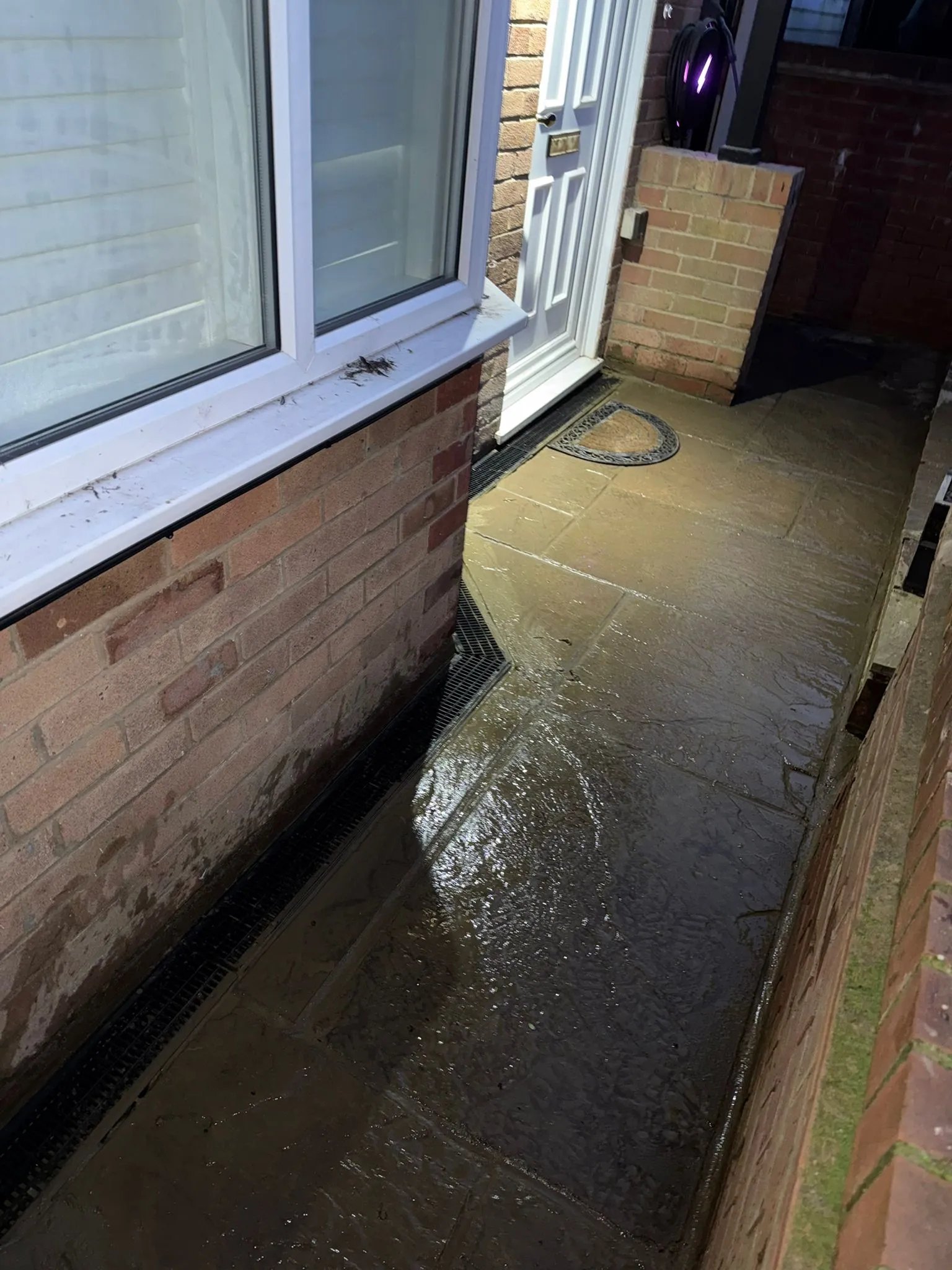 Blocked external channel drain causing flooding on a paved walkway at a property in Bournemouth.