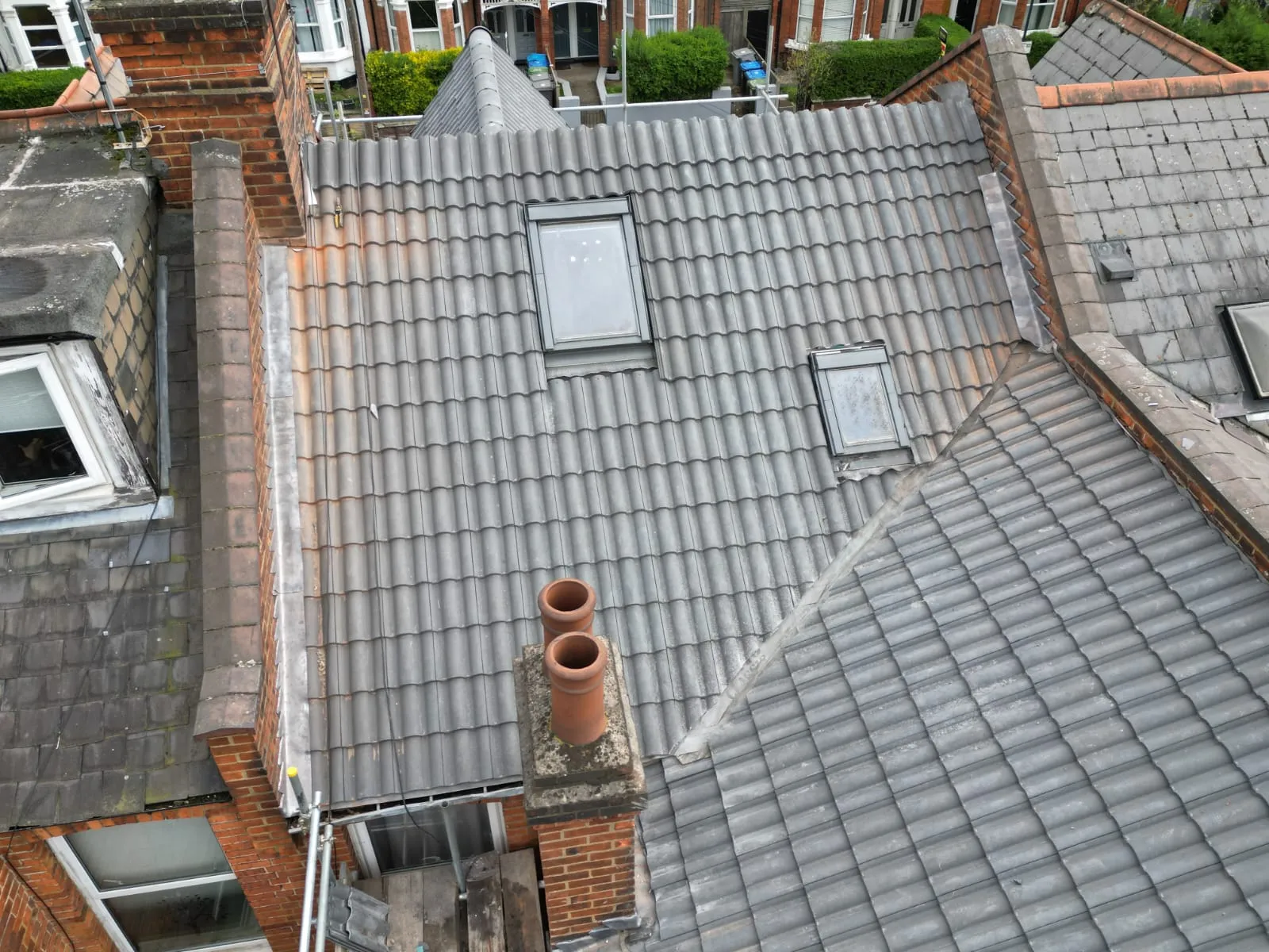 Overhead view of residential grey tiled pitched roofs with skylights, a brick chimney, and lead flashing.
